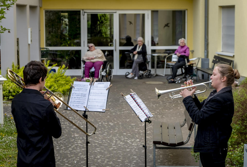 FILE - In this April 13, 2020 file photo, young musicians plays the trumpet, right, and trombone in the garden of a retirement and nursing home in Karben near Frankfurt, Germany. They played various pieces for the old people who are due to the coronavirus not allowed to leave the building. More than 50,000 people have died after contracting COVID-19 in Germany, a number that has risen swiftly over recent weeks as the country has struggled to bring down infection figures. (AP Photo/Michael Probst, File)