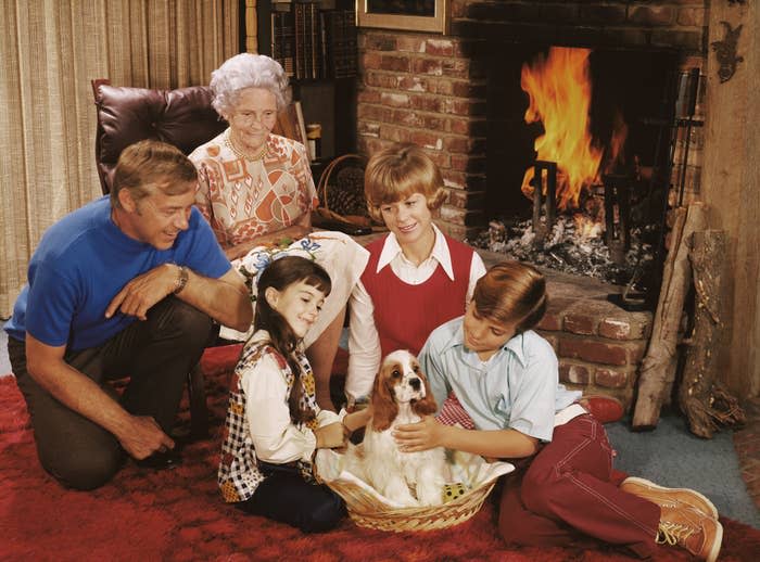 Adam West, Imogene Coca, and young actors pose around a fireplace with a dog in a cozy, vintage living room