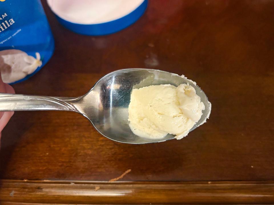 A metal spoonful of white vanilla ice cream with a blue container in the background