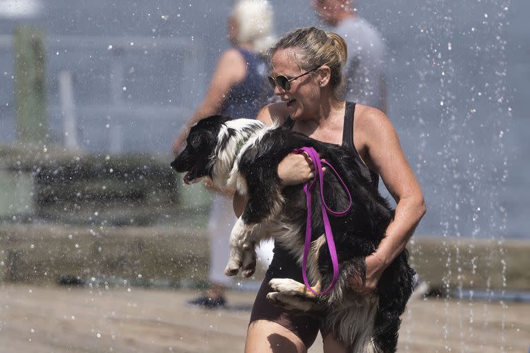 Una mujer lleva a su perro a través de una fuente de agua en el paseo marítimo de Halifax en Halifax, Nueva Escocia, el jueves 6 de julio de 2023. 
