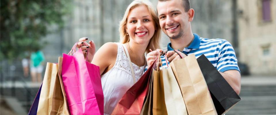 Young man and beautiful woman holding shopping paper bags and looking happy in town