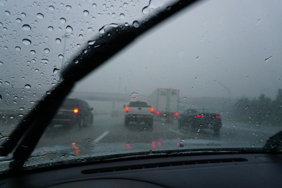 View from car's interior with raindrops on windshield, vehicles on a rainy highway ahead