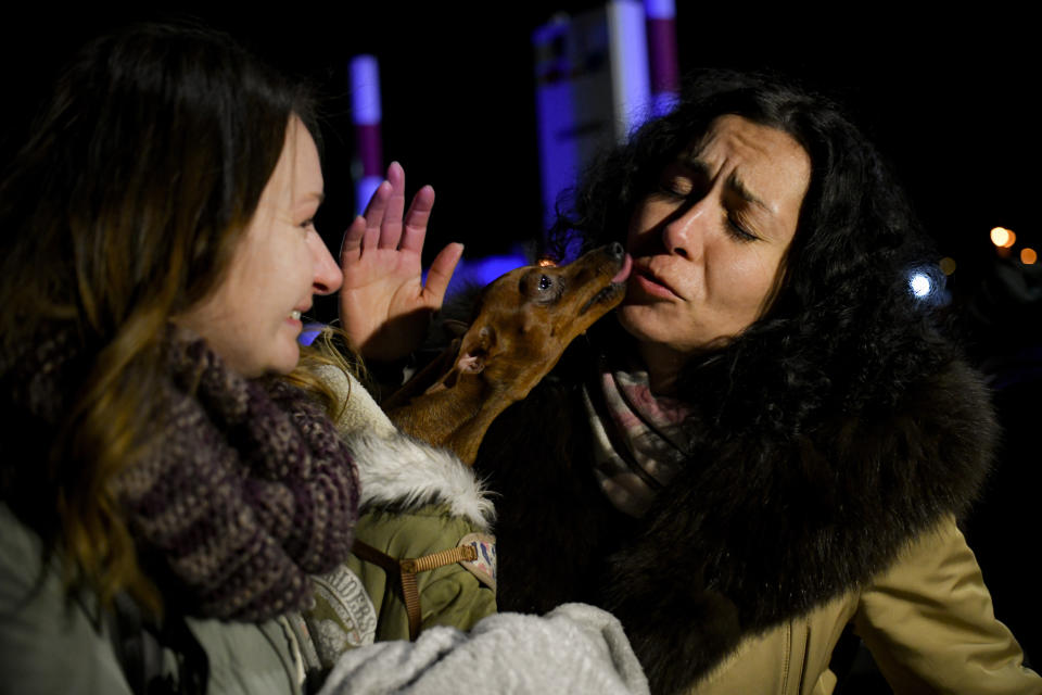 A dog named Josephine licks a Ukrainian woman reunited with her sister after crossing the border from Ukraine at the Romanian-Ukrainian border, in Siret, Romania, Friday, Feb. 25, 2022. (AP Photo/Andreea Alexandru)