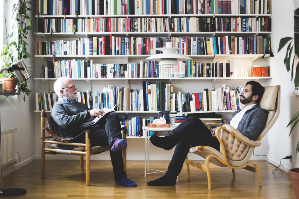 A therapist and client engaged in a conversation, seated across from each other in a room with a bookshelf