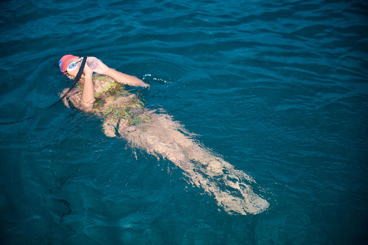 Prisha faces the sky as she lies in the sea while taking a drink from a water bottle