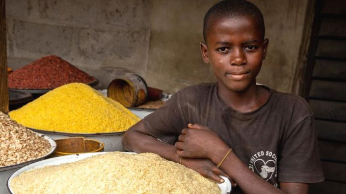 A young boy poses next to rice in his shop at the Ajara market