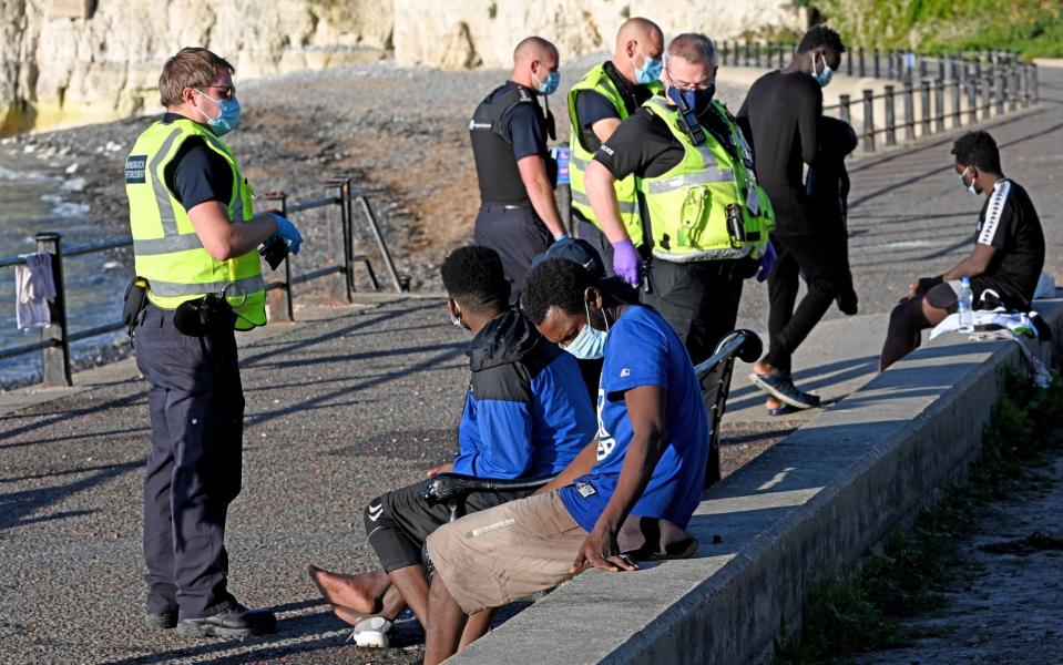 Migrants wearing face masks are talked to by police - Steve Finn