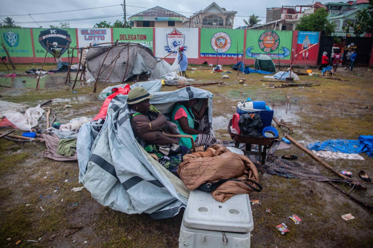 Two women take shelter after being hit by Tropical Storm Grace at an improvised refugee camp at Parc Lande de Gabion stadium after a 7.2-magnitude earthquake struck Haiti on Aug. 17, 2021, in Les Cayes, Haiti.