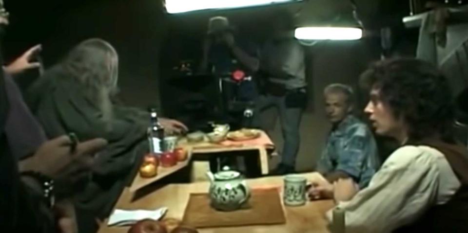 the cast sitting at the table while cameras film