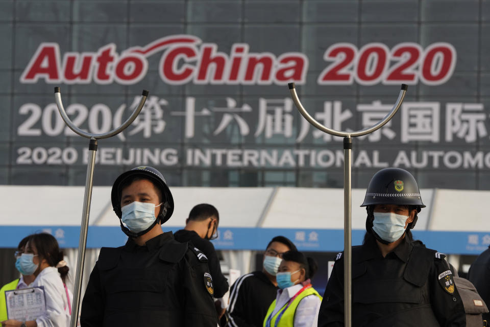 Security guards wearing masks and armed with restrainers stand guard at the entrance to the Auto China 2020 show in Beijing, China on Saturday, Sept. 26, 2020. The auto show, the first major in-person sales event for any industry since the coronavirus pandemic began, opens Saturday in a sign the ruling Communist Party is confident China has contained the disease. Still, automakers face intensive anti-virus controls including quarantines for visitors from abroad and curbs on crowd sizes at an event that usually is packed shoulder-to-shoulder with spectators. (AP Photo/Ng Han Guan)