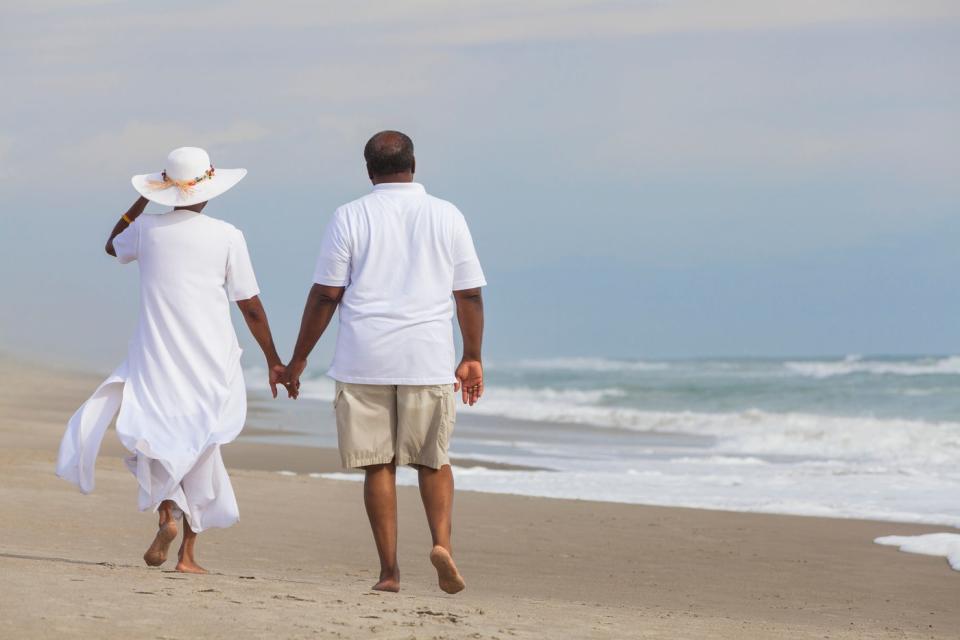 Two people walking down a beach holding hands.