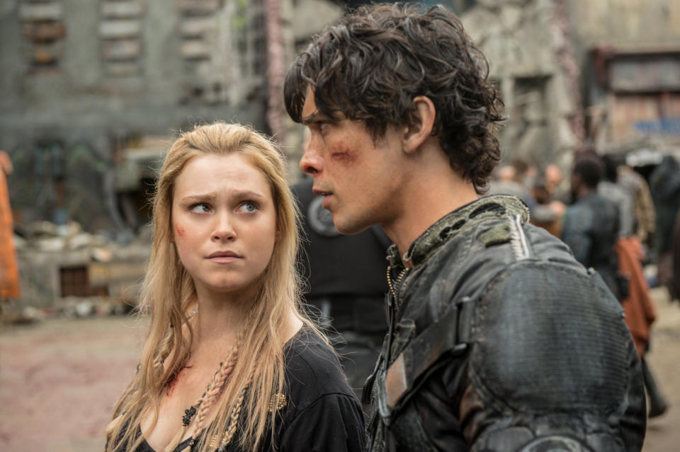 Eliza Taylor and Bob Morley, dressed in rugged, apocalyptic attire, look concerned in a scene from the TV show "The 100," set in a dystopian environment