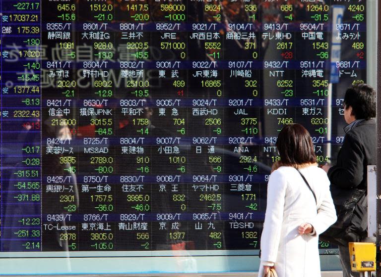 Pedestrians look at a share prices board in Tokyo on December 15, 2014