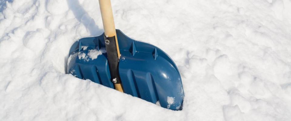 Snow shovel with a wooden handle in a snowbank after cleaning snow in the backyard
