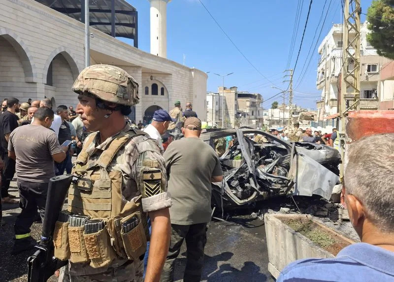 People and Lebanese army members stand near a burnt car after an Israeli strike on the outskirts of the southern port city of Sidon according to two Palestinian sources