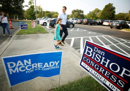 Dan McCready, Democratic candidate in the special election for North Carolina's 9th Congressional District, holds hands with his daughter Anna Glenn as they walk past campaign signs for him and his Republican opponent Dan Bishop in Charlotte, North Carolin