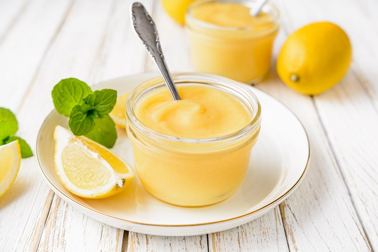 Delicious homemade tangy lemon curd decorated with fresh fruit in a glass jars on rustic wooden background