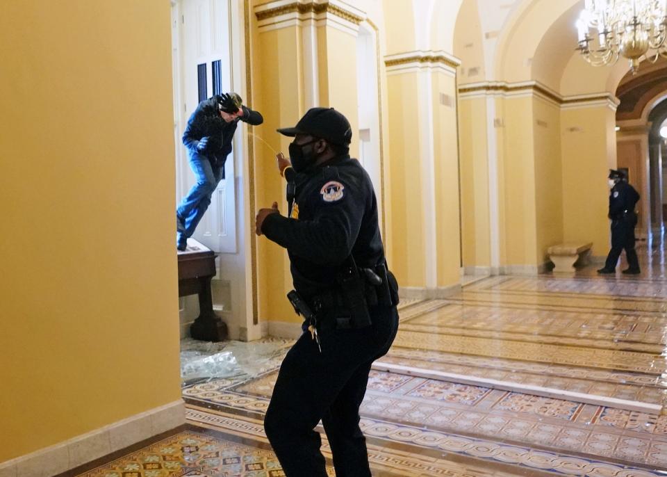 A Capitol police officer retreats as a rioter attempts to enter the building through a broken window, January 6, 2021.
