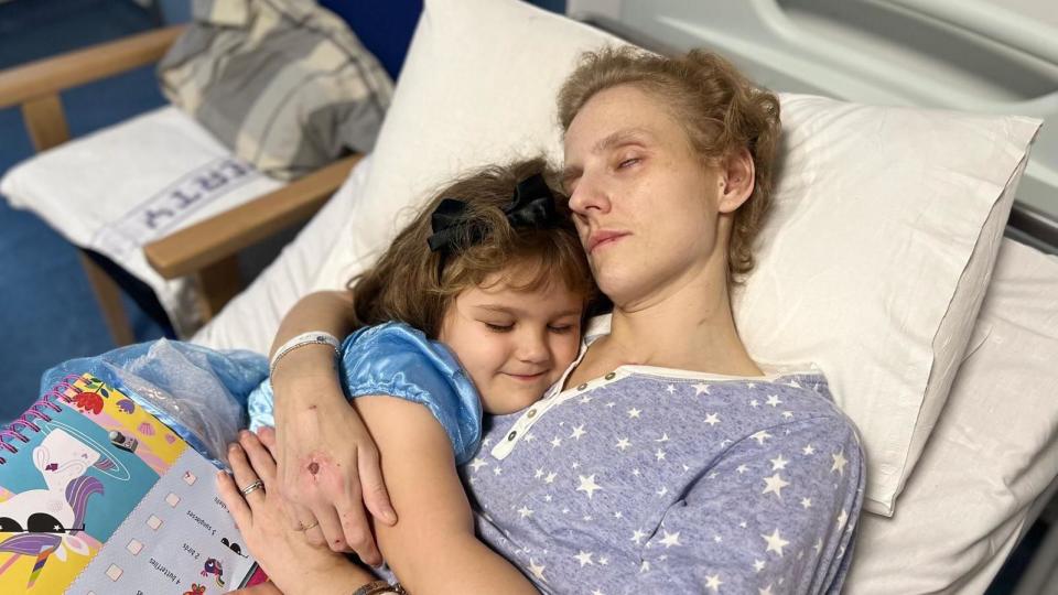 Poppy in her princess dress cuddling her mother in hospital