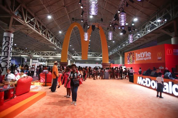 Golden Arches hanging from the ceiling of a convention hall over an empty carpet, with McDonald's booth at right.