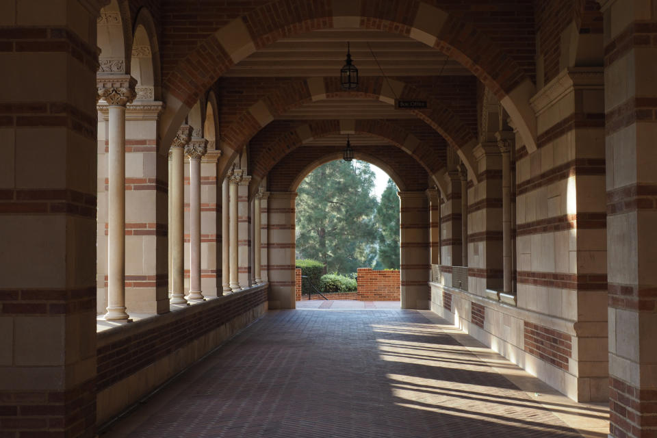 A serene, empty brick arcade with arches and columns, leading to a view of greenery and trees outside