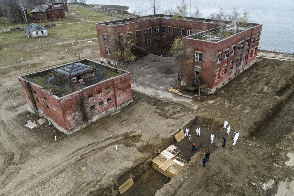 Workers wearing personal protective equipment bury bodies in a trench on Hart Island, Thursday, April 9, 2020, in the Bronx borough of New York. On Thursday, New York City’s medical examiner confirmed that the city has shortened the amount of time it will hold on to remains to 14 days from 30 days before they will be transferred for temporary internment at a City Cemetery. Earlier in the week, Mayor Bill DeBlasio said that officials have explored the possibility of temporary burials on Hart Island, a strip of land in Long Island Sound that has long served as the city’s potter’s field. (AP Photo/John Minchillo)