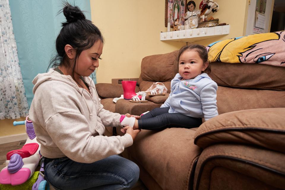 Belen Hernandez prepares her daughter to go outside with rain boots and a jacket on April 10.