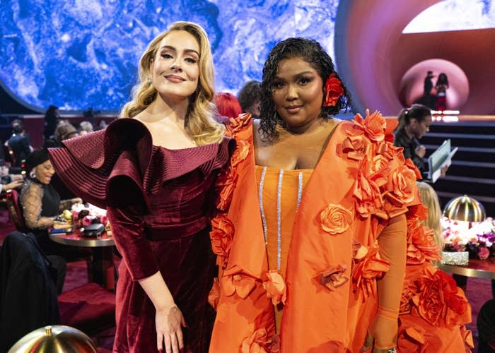 Adele and Lizzo stand next to each other as they have their photo taken by their table at the Grammys