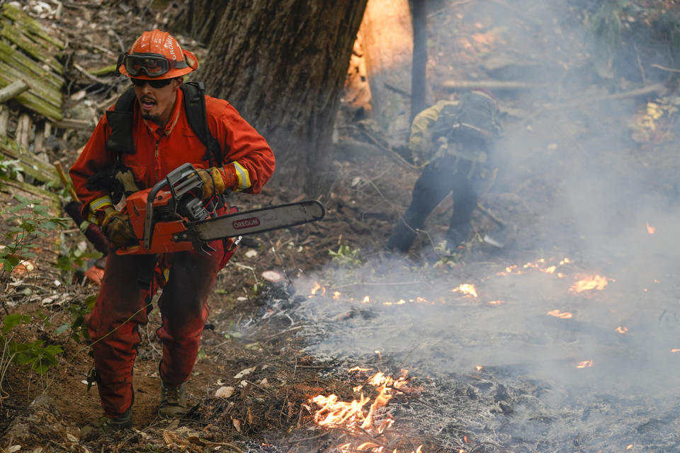 A member of a California Dept. of Corrections fire crew runs along a containment line with a chainsaw while fighting the CZU August Lightning Complex Fire, Friday, Aug. 21, 2020, in Bonny Doon, Calif. (AP Photo/Marcio Jose Sanchez)