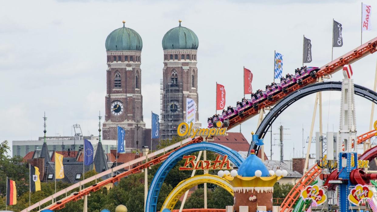 Oktoberfestbesucher fahren in einer Achterbahn auf dem Oktoberfest auf der Theresienwiese. Im Hintergrund ist die Frauenkirche in der Münchner Altstadt zu sehen. Foto: Matthias Balk