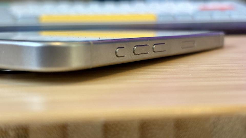 A grey titanium iPhone 15 Pro camera phone on a wooden desk