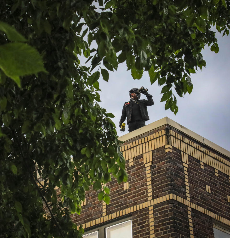 Obediah, a member of a neighborhood watch that started after the death of George Floyd in police custody sparked unrest, looks out from the roof of his home with binoculars, Tuesday June 2, 2020, in Minneapolis, Minn. A week of civil unrest has led some Minneapolis residents near the epicenter of the violence to take steps to protect their homes and neighborhoods. (AP Photo/Bebeto Matthews)