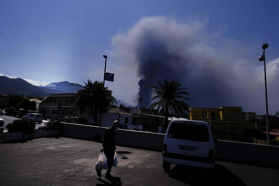 A man carries groceries from a supermarket as a volcano continues to erupt in El Paso on the canary island of La Palma, Spain, Saturday Oct. 9, 2021. A new lava flow has belched out from the La Palma volcano and it threatens to spread more destruction on the Atlantic Ocean island where molten rock streams have already engulfed over 1,000 buildings. The partial collapse of the volcanic cone overnight sent a new lava stream Saturday heading toward the western shore of the island. (AP Photo/Daniel Roca)