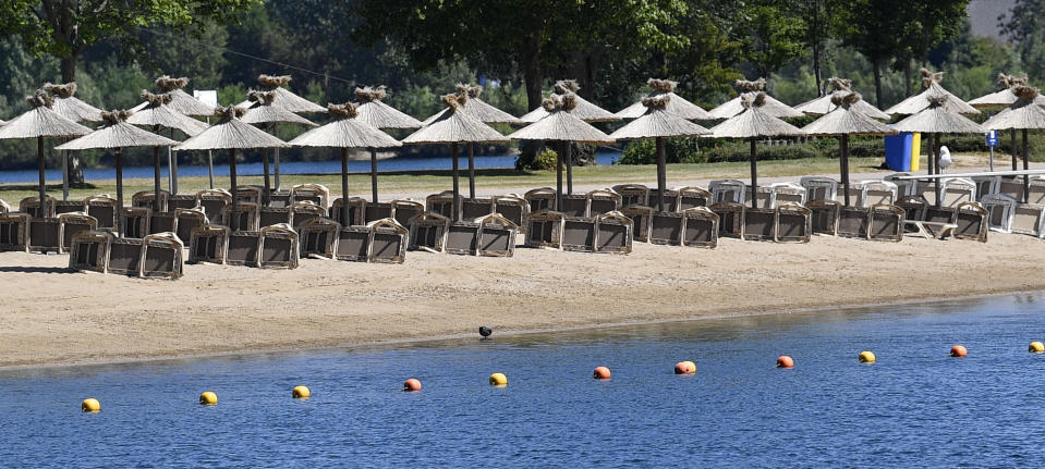 Parasols wait for tourists on a hot summer day at a lake in Xanten, Germany, Thursday, May 28, 2020. Germany's states, which determine their own coronavirus-related restrictions, have begun loosening lockdown rules to allow domestic tourists to return. (AP Photo/Martin Meissner)