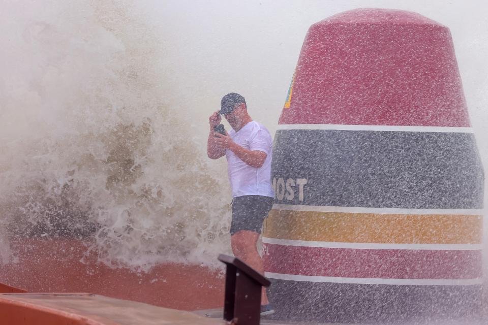 A man holds onto his hat as ocean spray from choppy Atlantic waves nearly surround him at the 'Southernmost Point' buoy in Key West on Thursday (EPA/SCOTT HALLERAN)