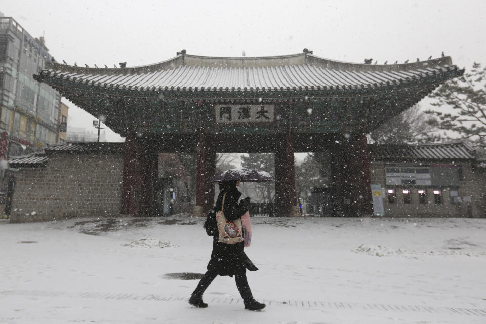 A woman wearing a face mask as a precaution against the coronavirus passes by the main gate of the Deoksu Palace in the snow in Seoul, South Korea, Tuesday, Jan. 12, 2021. (AP Photo/Ahn Young-joon)