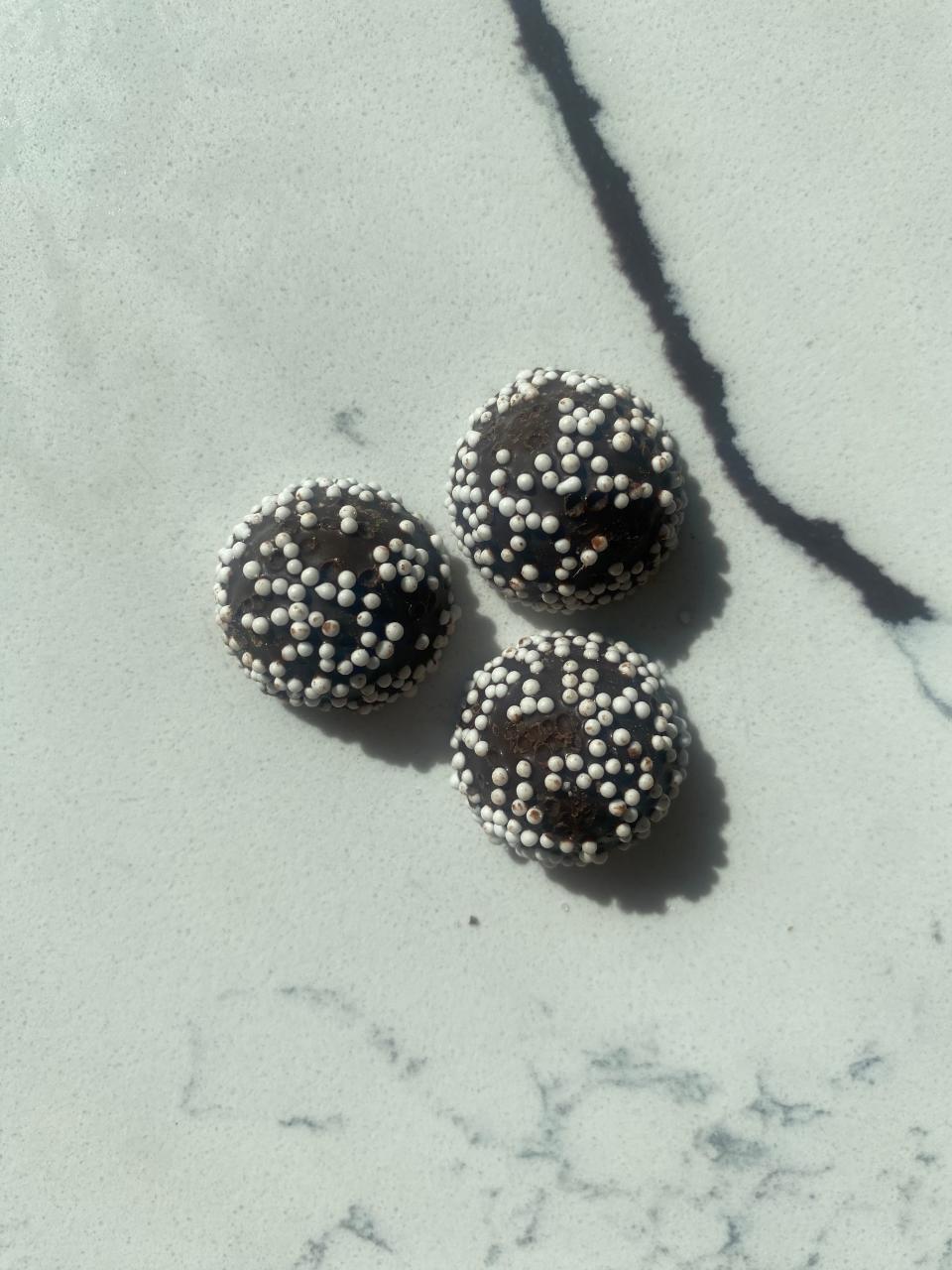 Three round chocolate truffles covered in white sprinkles resting on a marble surface