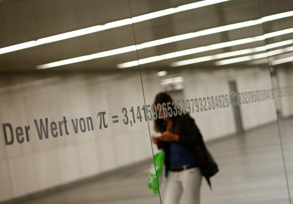 A woman is reflected in a mirror with an inscription reading “The value of Pi” and its numbers in Vienna  (AFP via Getty Images)