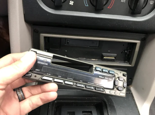 Hand removing a car's stereo system from the dashboard