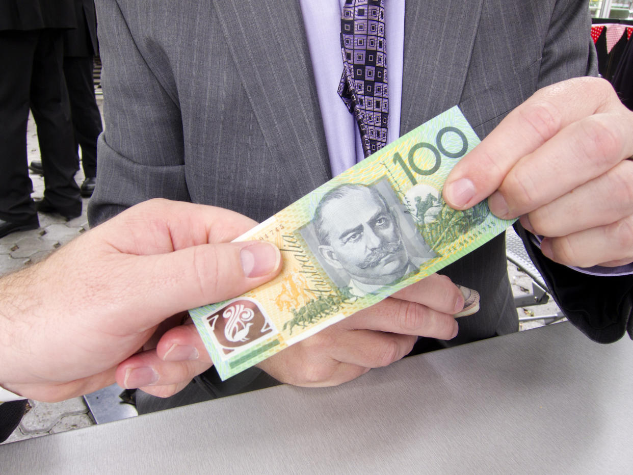 A man in a suit is holding a $100 note. Another man is holding the other side of the note. 