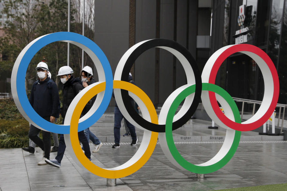 FILE - In this March 4, 2020, file photo, people wearing masks walk past the Olympic rings near the New National Stadium in Tokyo. Local Japanese sponsors have chipped in a record $3.3 billion to organize the postponed Tokyo Olympics. That's almost 60% of the income for the privately funded operating budget. With the games delayed for a year, sponsors will be asked to sign up again. (AP Photo/Jae C. Hong, File)