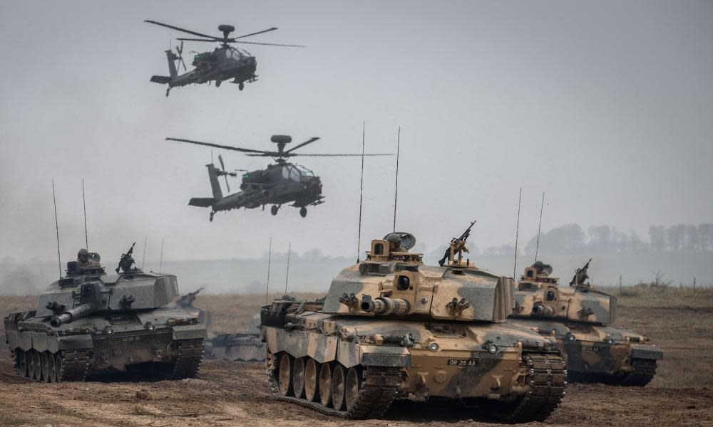 Apache helicopters hover above a column of Army vehicles on exercise on Salisbury Plain.