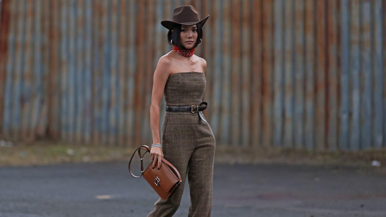 a person in a jumpsuit and cowboy hat holding a purse