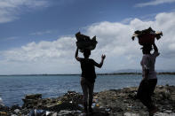 Women carry buckets of trash to the shore on the sidelines of a market in Cap-Haitien, Haiti, Thursday, July 22, 2021. The city of Cap-Haitien is holding events to honor slain President Jovenel Moïse on Thursday ahead of Friday’s funeral. (AP Photo/Matias Delacroix)