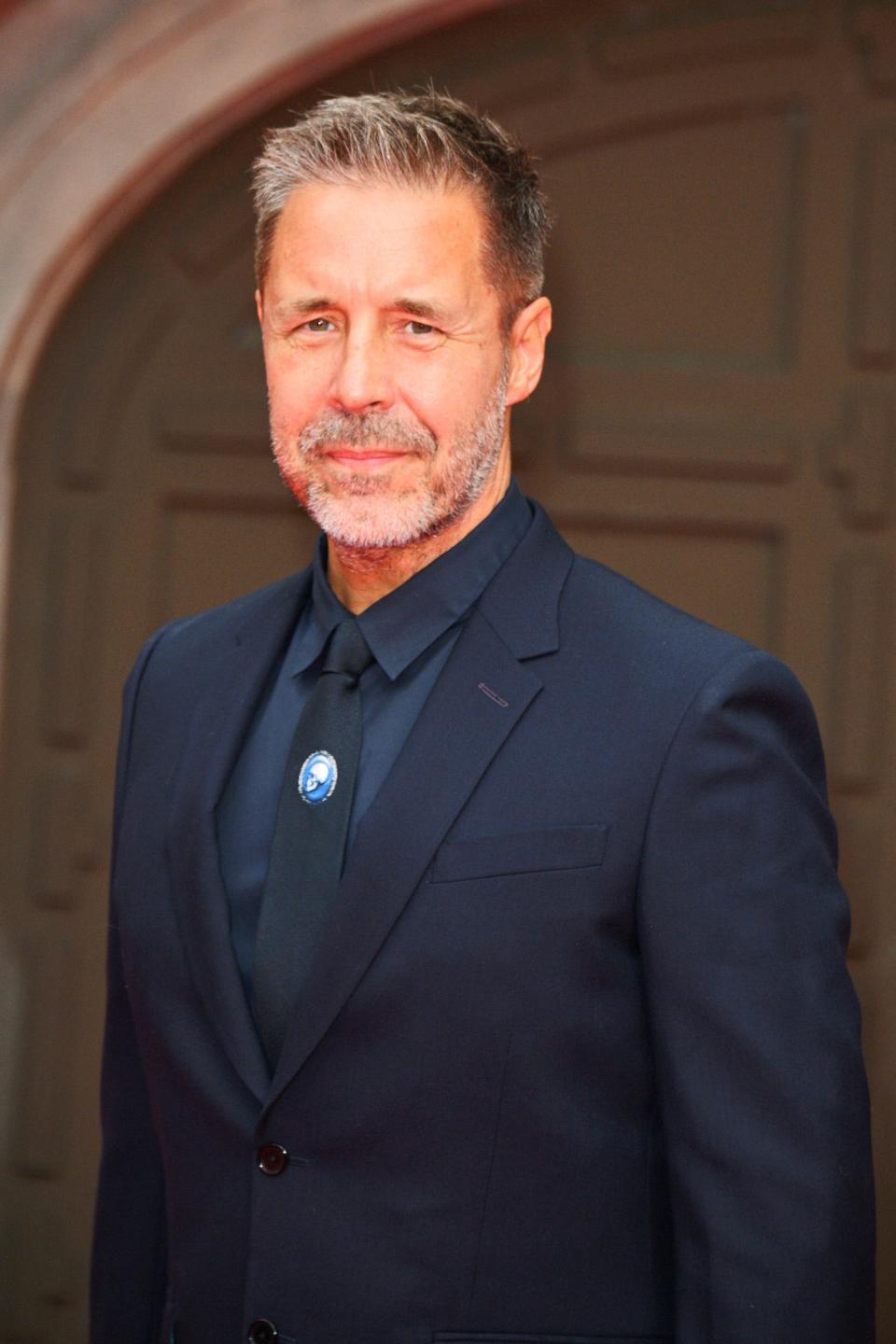 A white man with short graying hair wearing a navy suit and navy shirt.