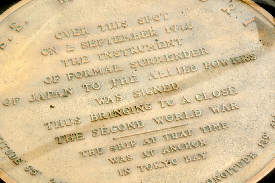 In this Aug. 11, 2020 photo, a plaque marks the spot where World War II surrender documents were signed on the USS Missouri Memorial in Pearl Harbor, Hawaii. Several dozen aging U.S. veterans, including some who were in Tokyo Bay as swarms of warplanes buzzed overhead and nations converged to end World War II, will gather on the battleship in Pearl Harbor in September to mark the 75th anniversary of Japan's surrender. (AP Photo/Caleb Jones)