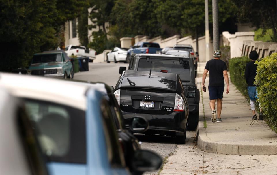 Two people walking on the sidewalk near parked cars