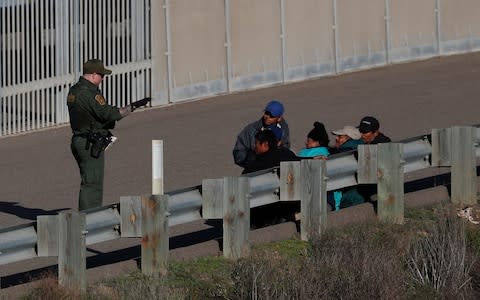 Honduran migrants sit after crossing the U.S. border wall and turning themselves into U.S. border patrol agents in San Diego - Credit: AP