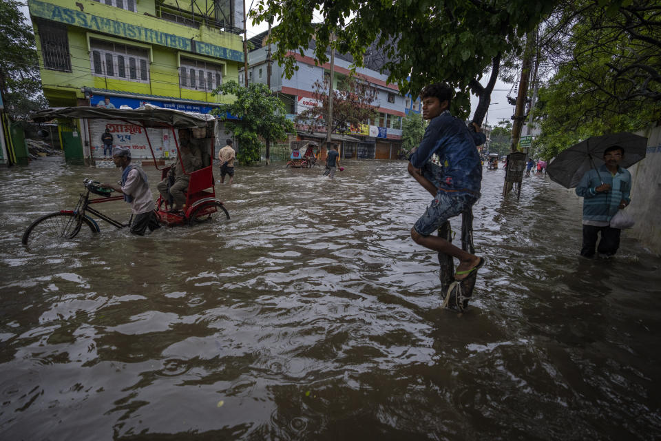 Personas caminan por un camino inundado después de lluvias fuertes en Gauhati, en el estado indio de Assam, el 14 de junio de 2022. (AP Foto/Anupam Nath)