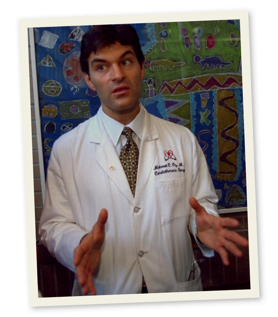 Dr Oz gestures with his hands in front of him while wearing a white doctor's jacket and standing in front of a wall with simple children's illustrations